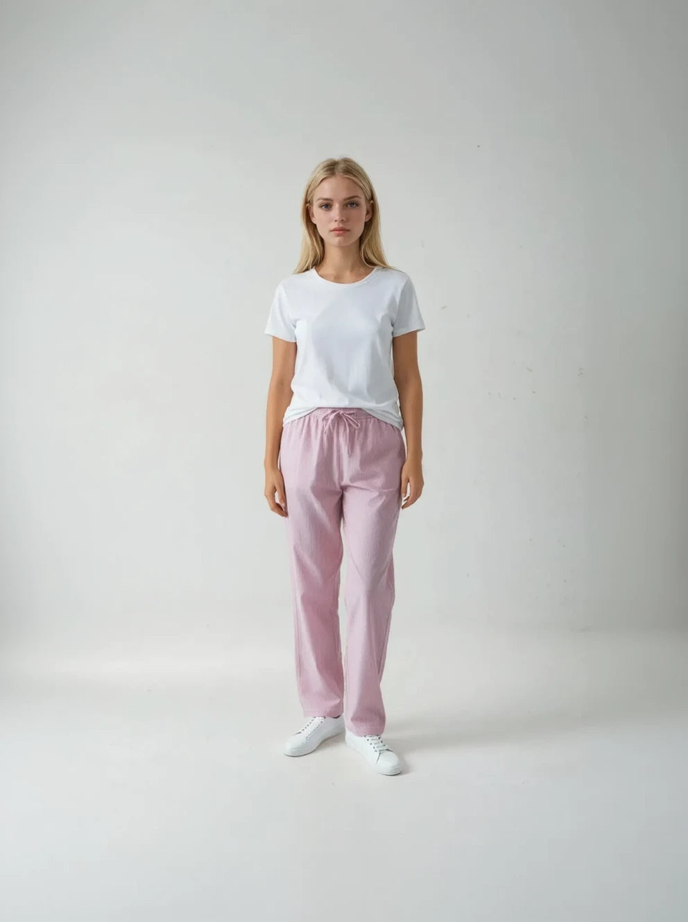 Woman wearing a white t-shirt and pink pants on a plain background
