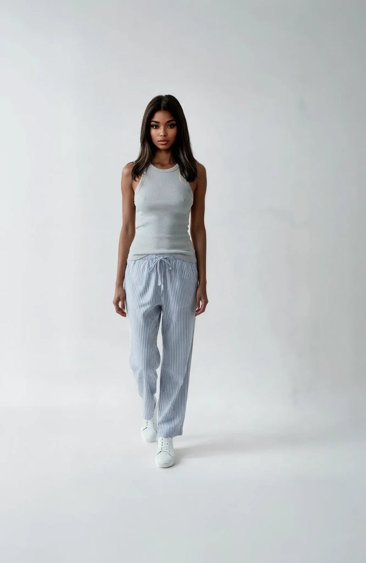 Woman wearing a gray tank top and light blue striped pants on a white background